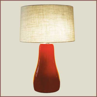 A Red Lamp With a Beige Shade on a Wooden Table